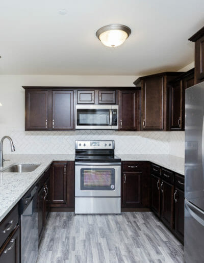 modern kitchen with gray wood floors, stone countertops, and stainless appliances