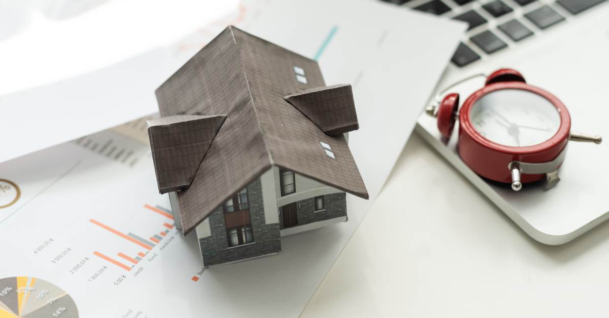 house model with alarm clock on top of paperwork